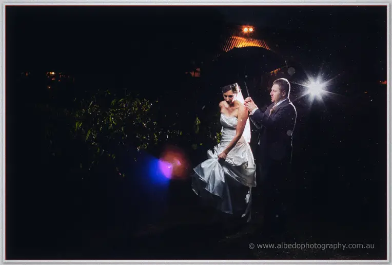 Felicity in a strapless gown and Mark stand together at night adjusting her veil under a warm farm light