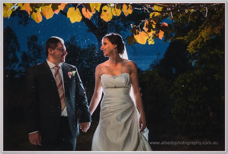 Hand in hand under autumn vines, Felicity and Mark smile at each other at nightfall.