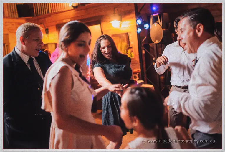 Guests of all ages dance and laugh beneath the barn's warm party lights.