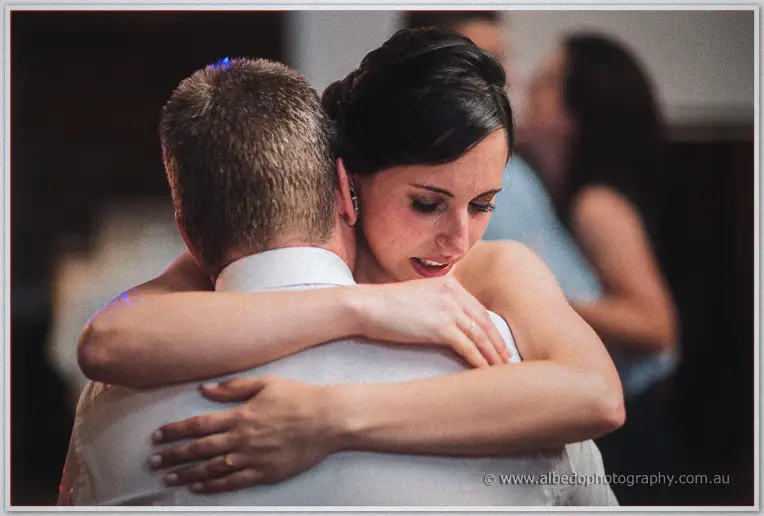 Felicity embraces a guest closely on the dance floor, eyes closed.