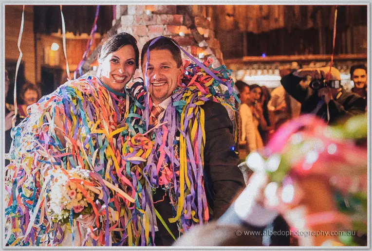 Felicity and Mark grin, draped in colourful streamers amid the party crowd.