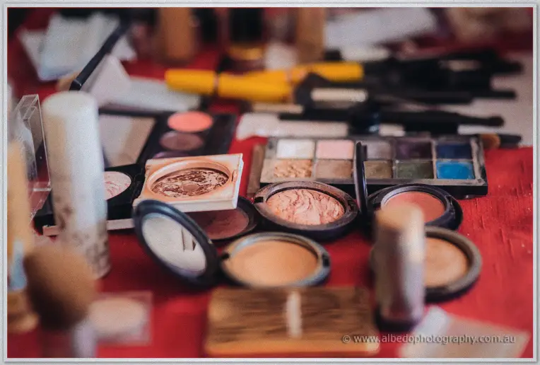 Loose makeup palettes, brushes and powder compacts spread across a red table during bridal preparations.