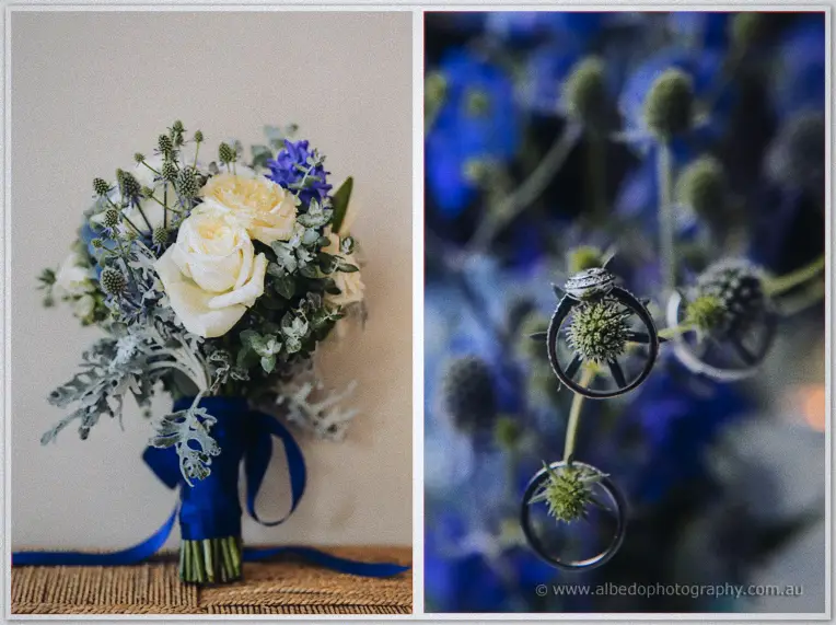 Kristyn's bouquet of cream roses and blue thistles beside rings threaded through spiky blue blooms.