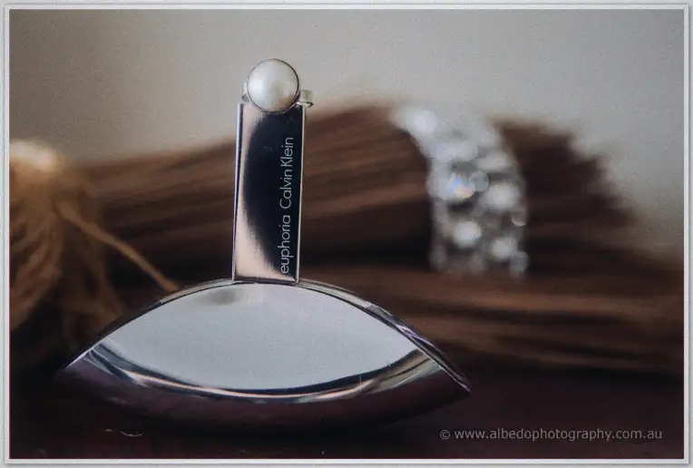 A pearl-topped perfume flacon glints beside a jewelled bracelet in soft morning light.