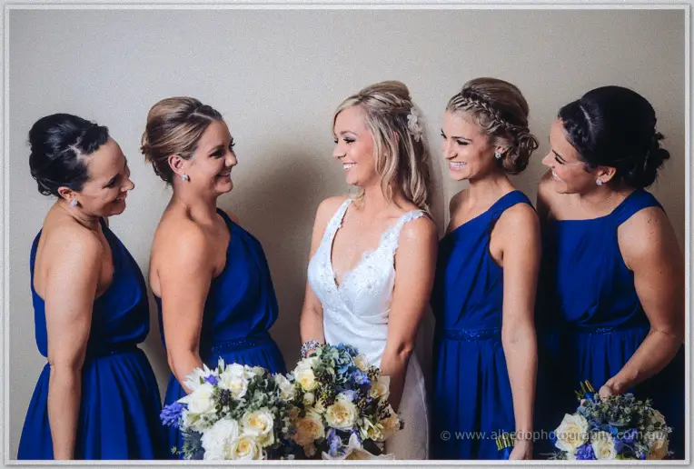 Kristyn and four bridesmaids in cobalt dresses laugh together holding white and blue bouquets.