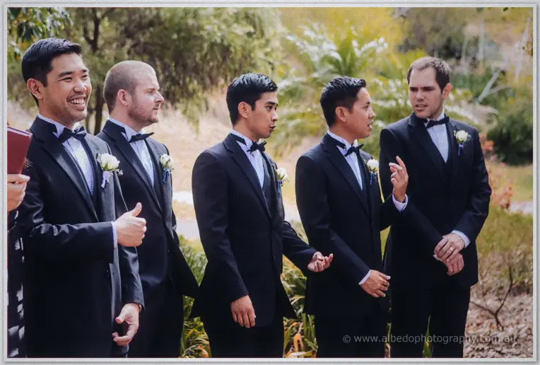 Chris and his groomsmen in black tuxedos share a last laugh before the ceremony beneath the trees.