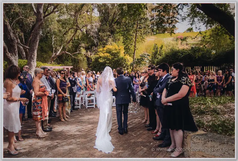 Kristyn and her father walk down the aisle as guests line the leafy South Perth garden ceremony.