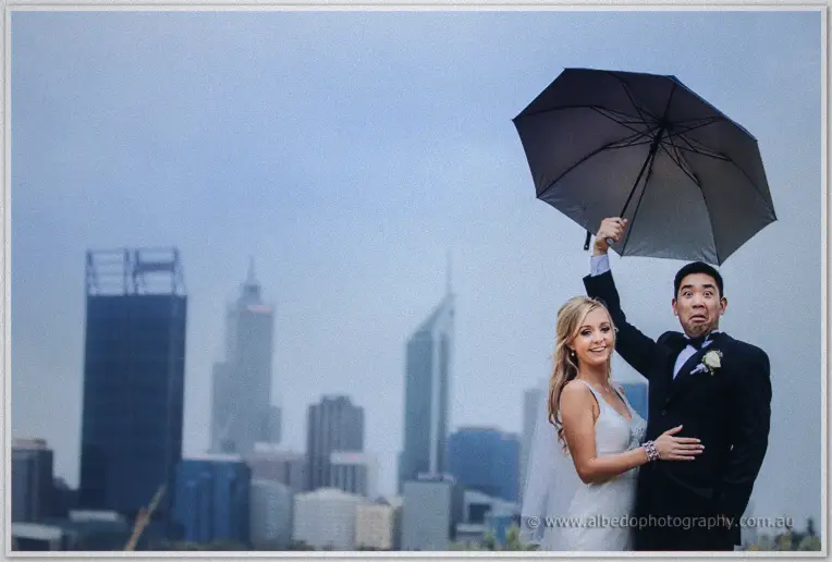 Chris holds an umbrella high against the misty sky as he and Kristyn pose before the Perth skyline