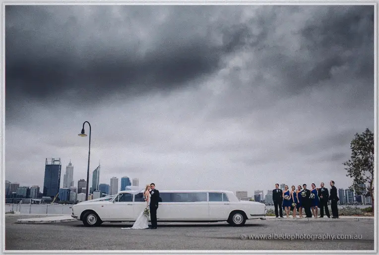 Kristyn and Chris kiss beside their white stretch limousine as storm clouds gather over the Perth skyline