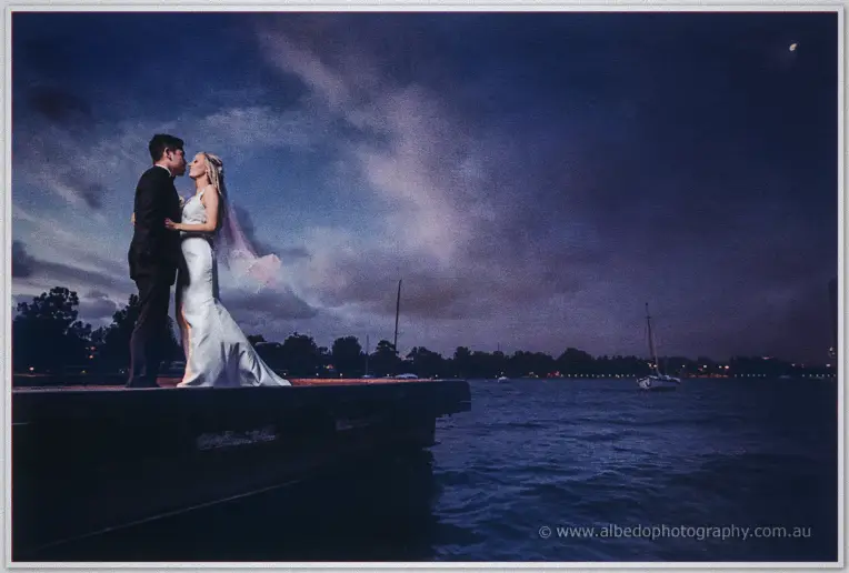 Kristyn and Chris kiss on a jetty at dusk in South Perth, veil drifting under a deep blue twilight sky.