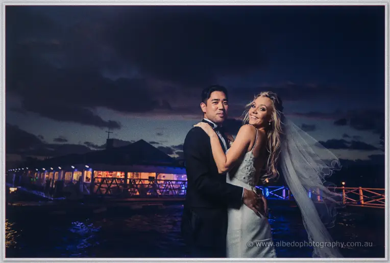 Kristyn's veil streams in the night breeze as the couple smile before the illuminated Acqua Viva pavilion