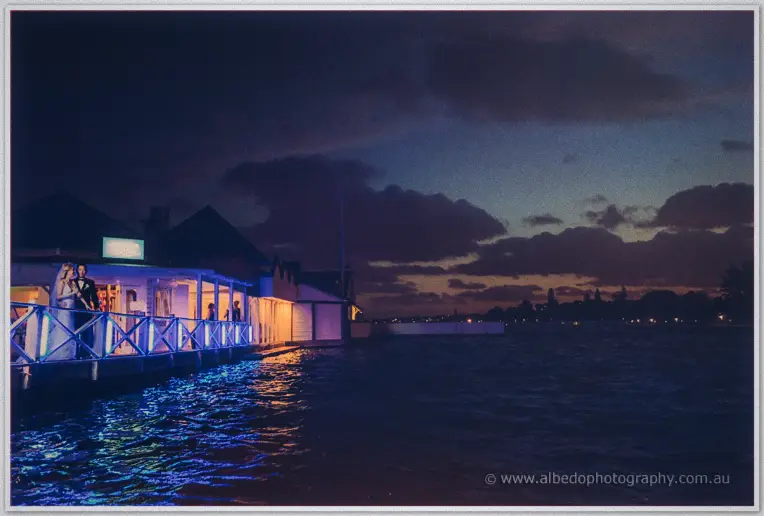 Blue-lit decking leads to the glowing Acqua Viva pavilion where the newlyweds stand beside the dark water