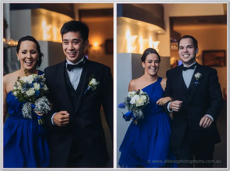 Smiling bridesmaids in cobalt gowns walk arm in arm with groomsmen in bow ties into the warmly lit venue