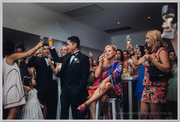 Guests raise their champagne flutes in a cheer around Chris amid the lively reception crowd