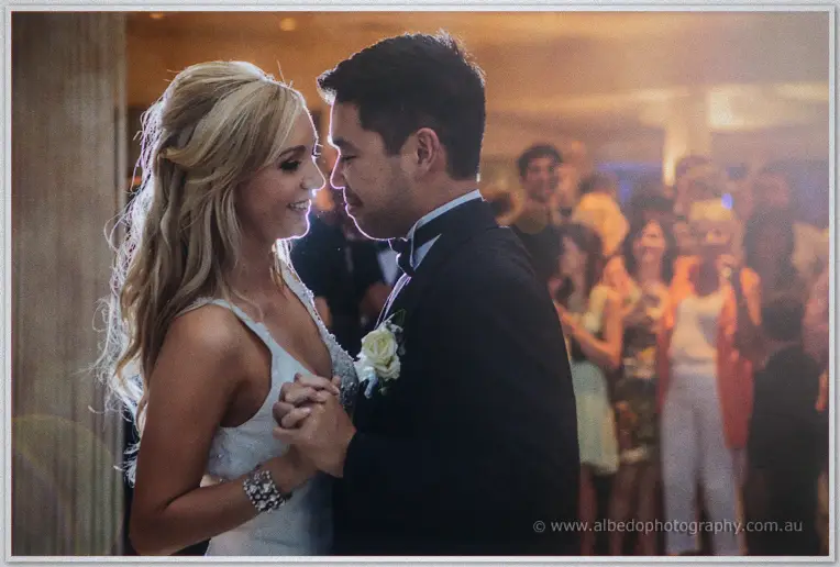 Foreheads nearly touching, Kristyn and Chris share their first dance as guests watch, blurred behind them