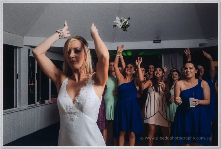 Kristyn hurls her bouquet over her shoulder toward the waiting bridesmaids packed beneath the pavilion ceiling
