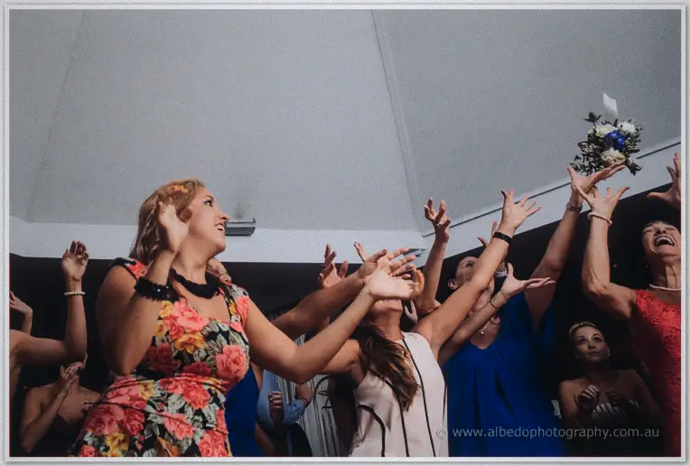 Guests leap and stretch toward the tumbling blue-and-white bouquet as laughter fills the reception room
