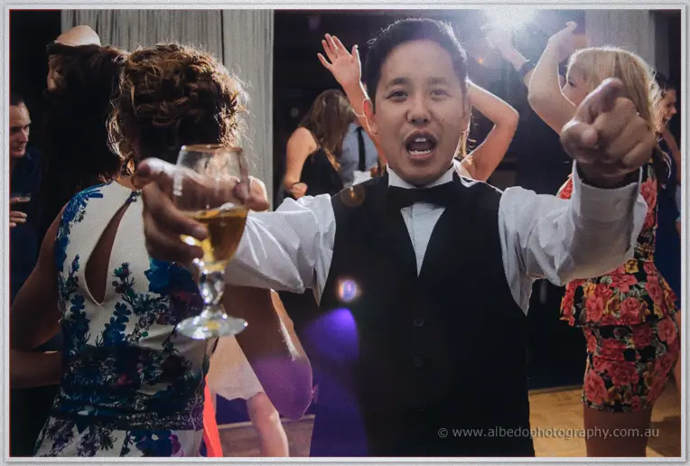 Chris sings along pointing at the camera, drink raised, as dancing guests crowd the purple-lit floor