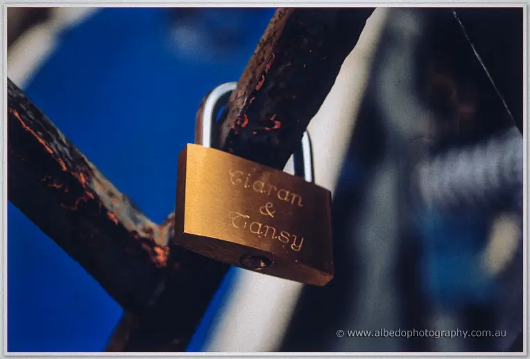 A brass love lock engraved Ciaran and Tansy clasped shut on a weathered rusted chain