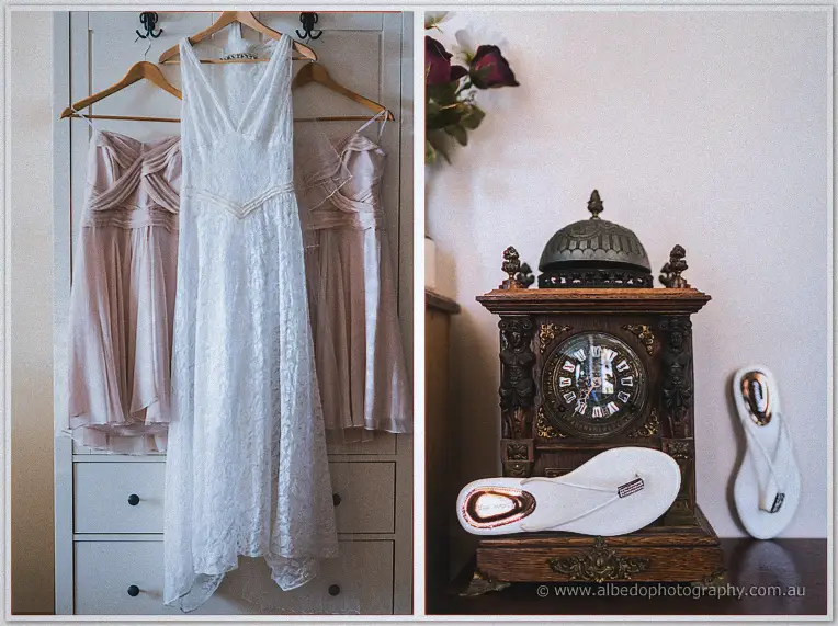 The lace bridal gown hangs between blush bridesmaid dresses beside white thongs and a vintage clock