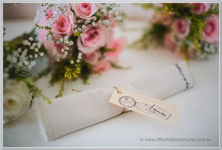 Pink rose posies and a twine-tied guest favour with a luggage tag wait on a white table