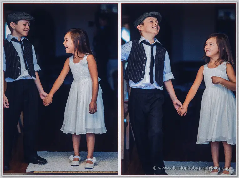 The page boy leads the laughing flower girl by the hand across a rug in soft window light