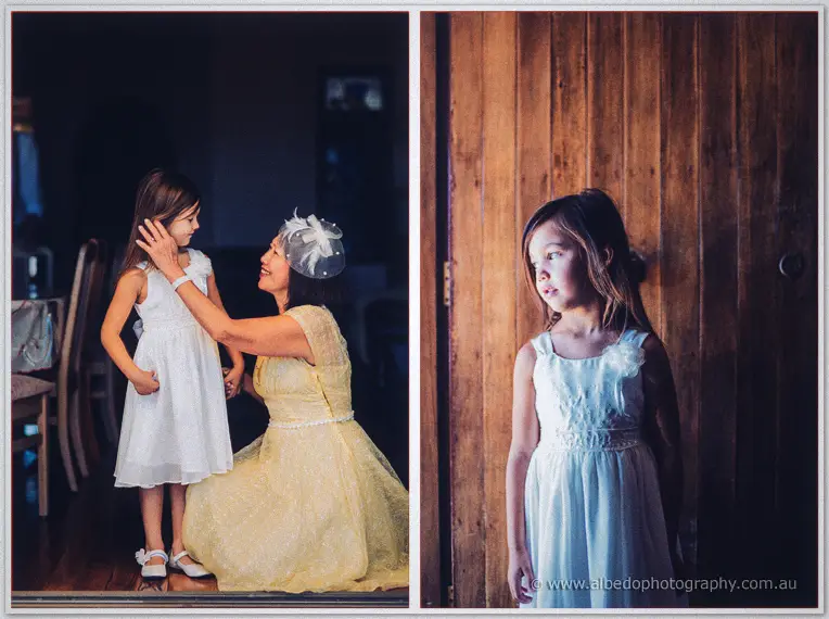 A grandmother in a lemon lace dress adjusts the flower girl's hair before she pauses by a timber wall