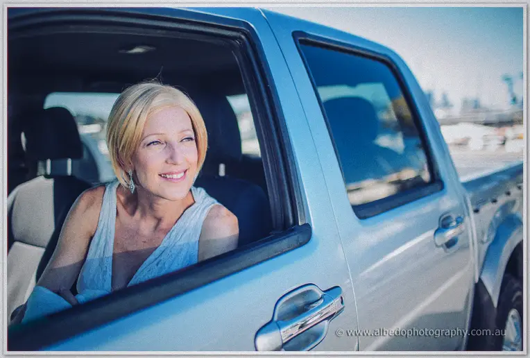 A smiling blonde guest in a white top leans from the window of a silver ute at the boat ramp