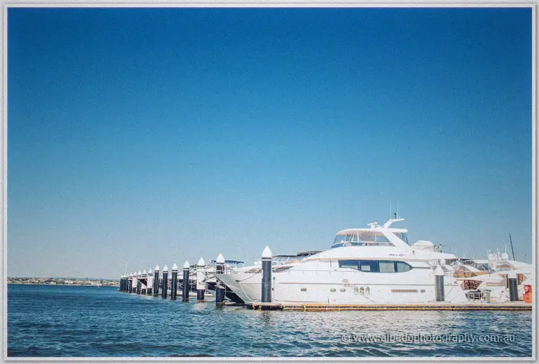Luxury motor yachts line the marina pontoons beneath a vast blue sky across calm water