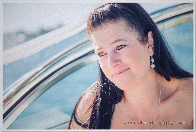 A dark-haired bridesmaid in pearl earrings gazes wistfully from the boat in bright sun