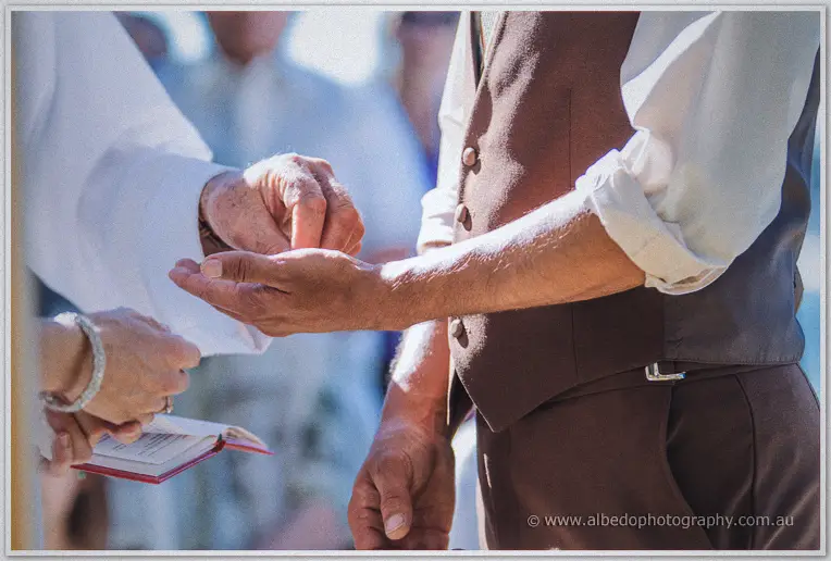 Close on the celebrant placing the ring on Ciaran's open palm during the riverside ceremony