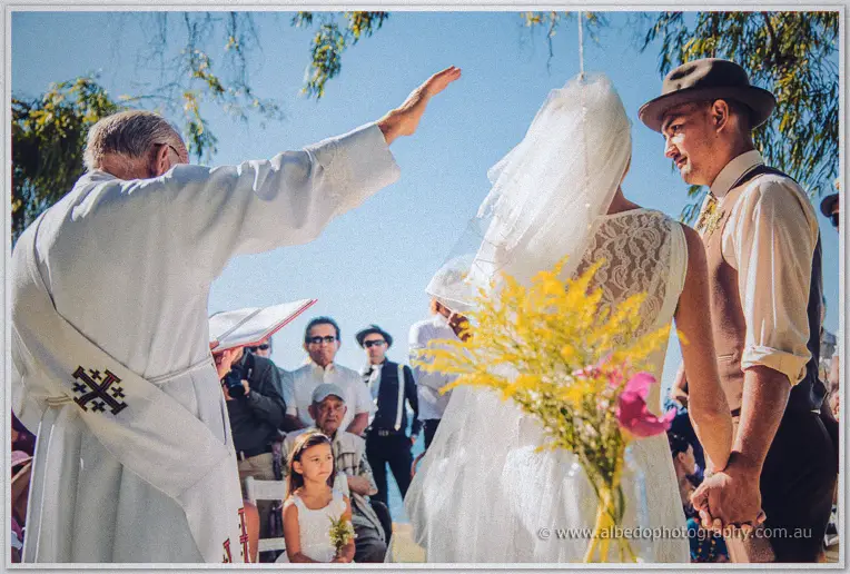 The celebrant raises his arm in blessing as Tansy and Ciaran hold hands beneath blue sky