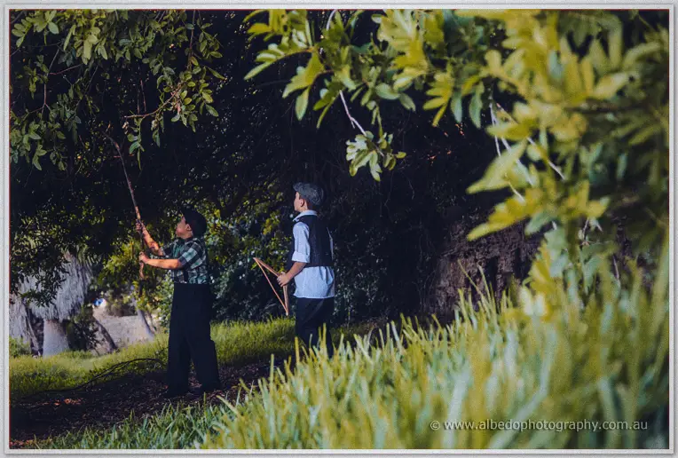 Two boys in vintage waistcoats play with sticks in the shadowed trees beside the picnic