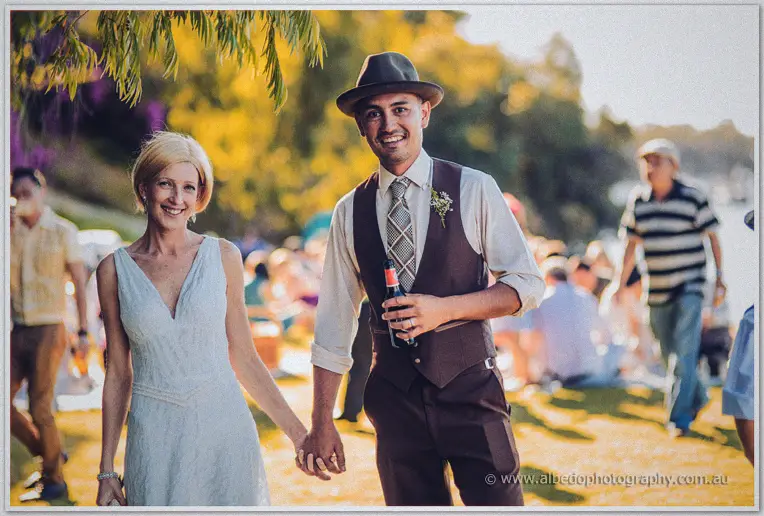 Ciaran holds a beer and Tansy's hand while walking through the golden picnic crowd