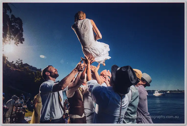 Groomsmen toss the bride skyward against a deep blue dusk above the river