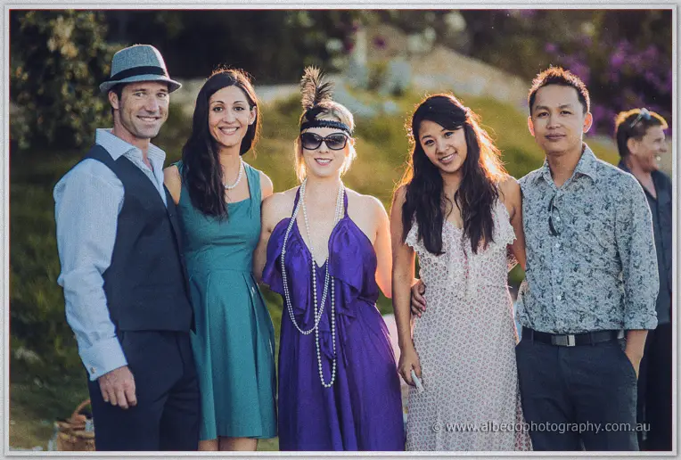 Five wedding guests in flapper hats and pearls line up smiling in the evening sun