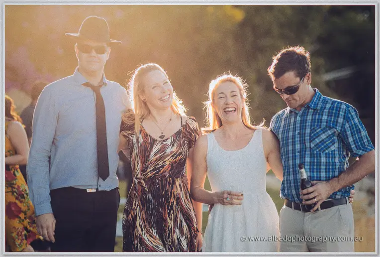 Four guests laugh together in the last sunset light during the riverside picnic wedding