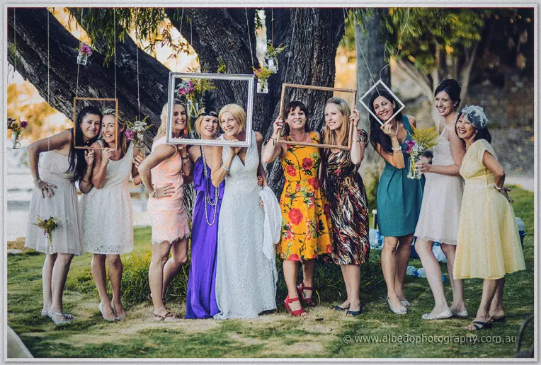 The bride and her friends pose with hanging picture frames under the willow at dusk