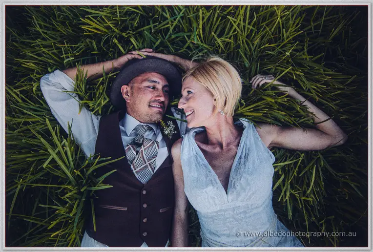 Tansy and Ciaran lie back in tall grass smiling at each other from above