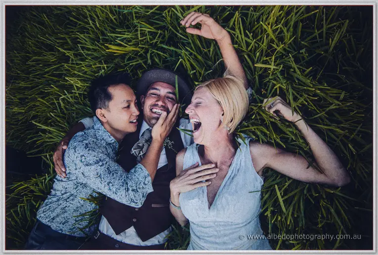 Friends pile into the grass with the laughing groom as the bride howls beside them