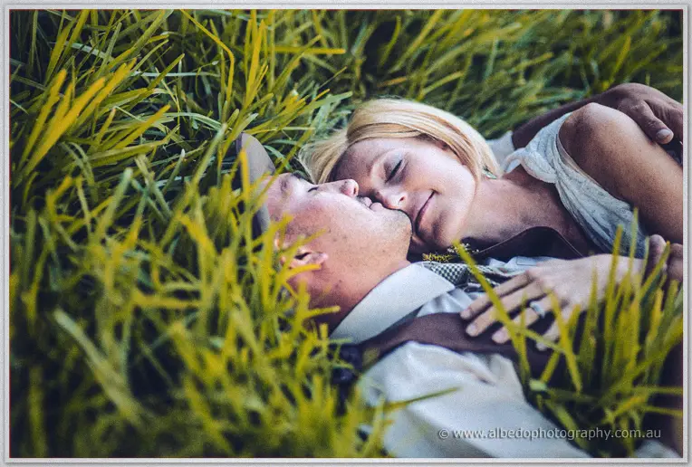 Ciaran and Tansy rest cheek to cheek among sunlit grass blades in a quiet close-up