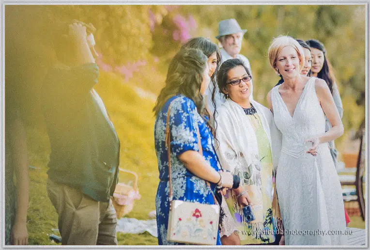 The bride in white chats warmly with guests in the golden picnic light at Mosman Park
