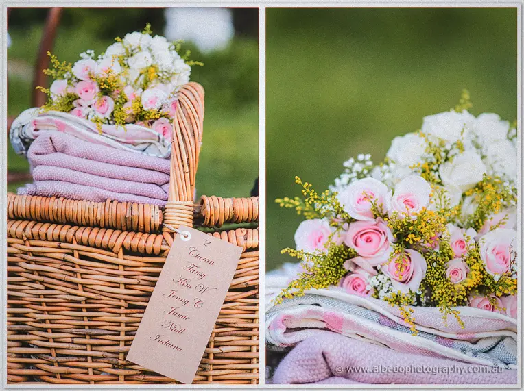 A picnic basket holds folded blankets topped with pink and white roses in the park sunshine
