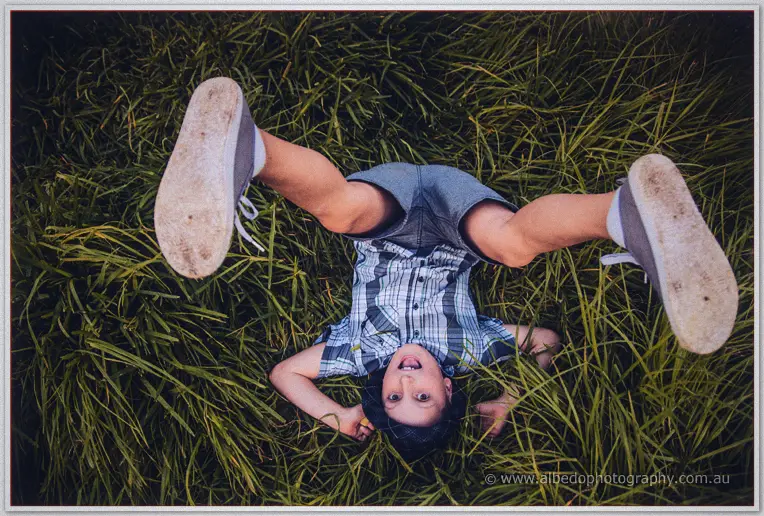 A boy in a checked shirt kicks his sneakers skyward as he tumbles into the long grass