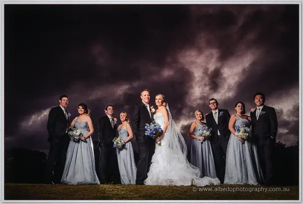 Sarah and Nathan front a formal bridal party lineup beneath a bruised purple storm sky