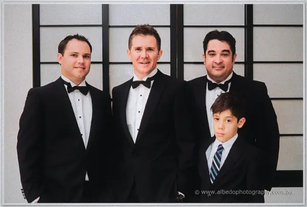 Three groomsmen and the page boy pose in tuxedos against a black-framed shoji screen wall