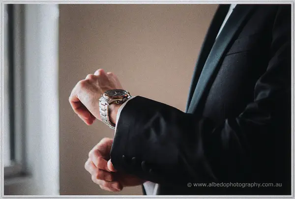 Close view of a silver wristwatch being adjusted below a crisp white shirt cuff and dark suit sleeve