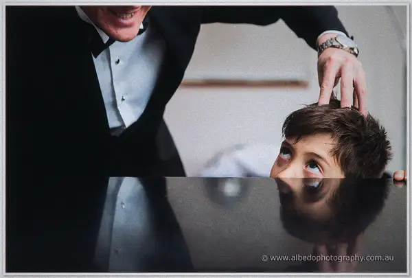 Groom gently ruffles the page boy's hair as the boy peeks up over the piano edge