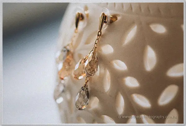 Crystal teardrop earrings dangle in soft light against a carved white ceramic vase