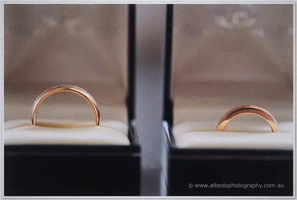 Two gold wedding bands rest on cream velvet inside matching dark ring boxes